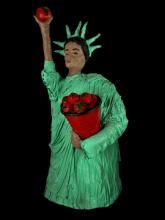 Statue of liberty made out of papier-mache, holding a bucket of tomatoes with one arm and holding a tomato up with the other
